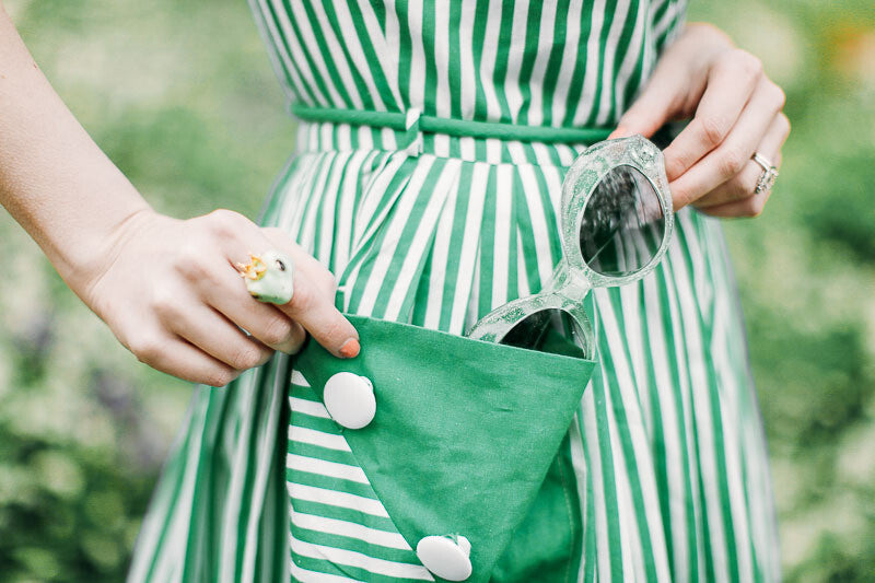 A woman holding a green pocket showcasing a frog prince ring and stylish sunglasses.