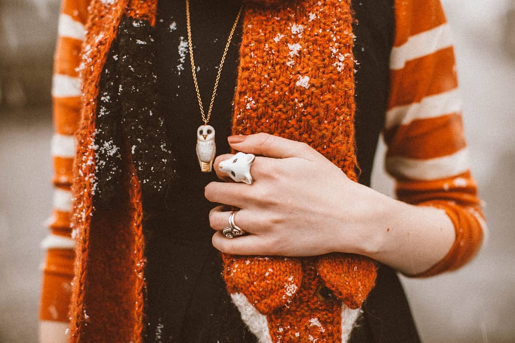 Close-up of a person wearing a white fox ring and owl whistle necklace in a cozy outfit.