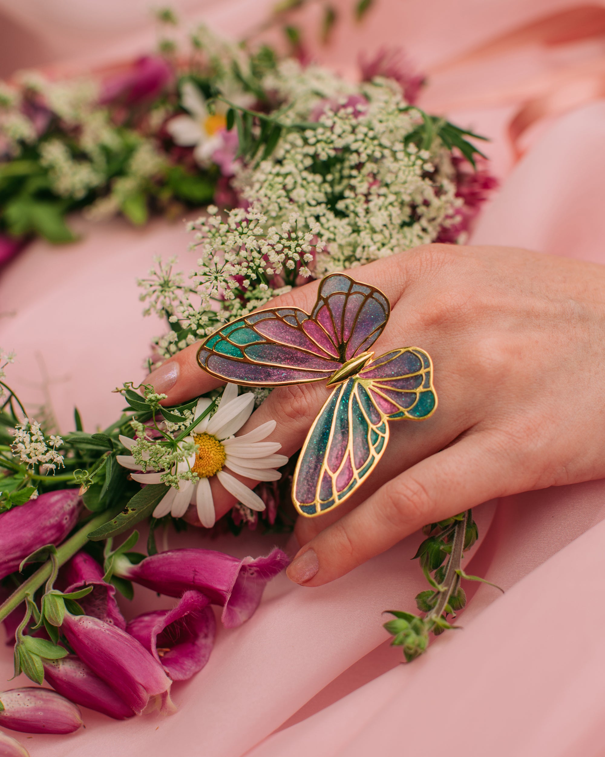 Colorful butterfly ring on a hand surrounded by flowers