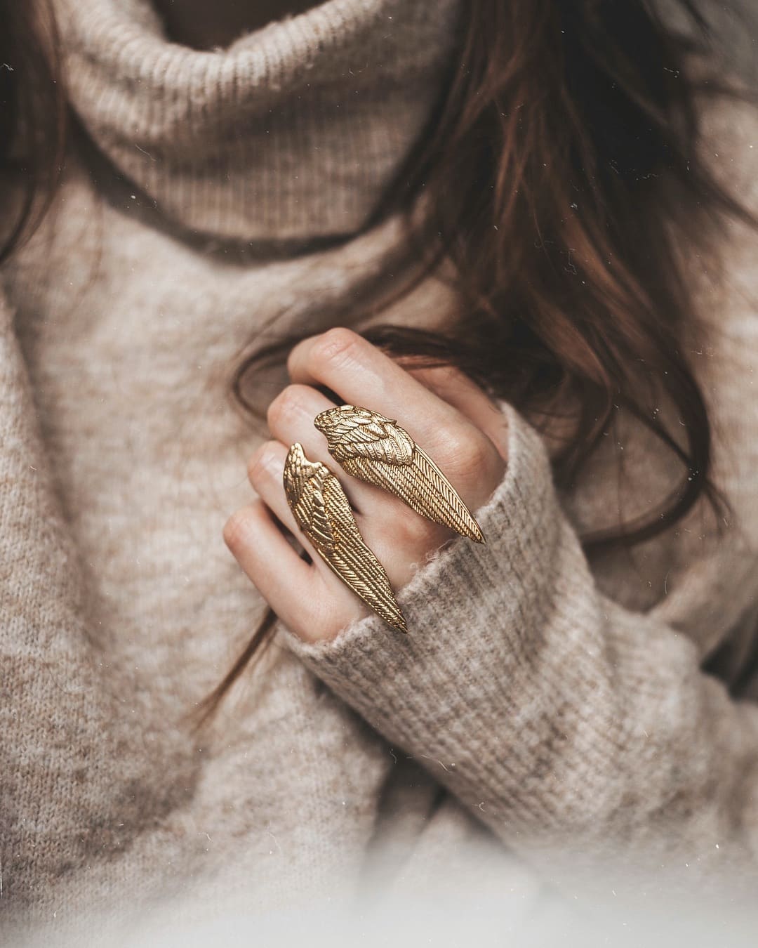 Close-up of a hand wearing a wing-shaped ring in a cozy sweater