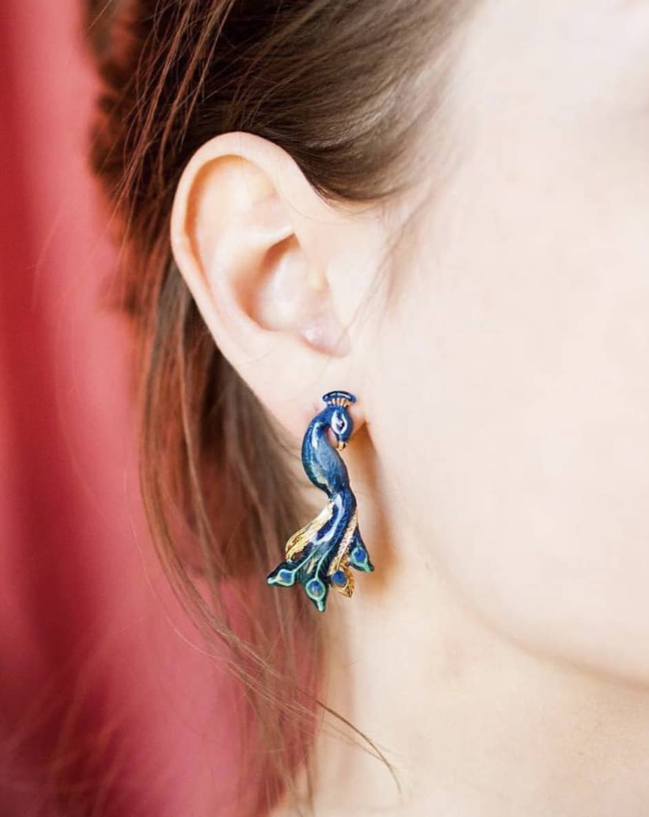 Close up of beautiful peacock earring worn on person's ear