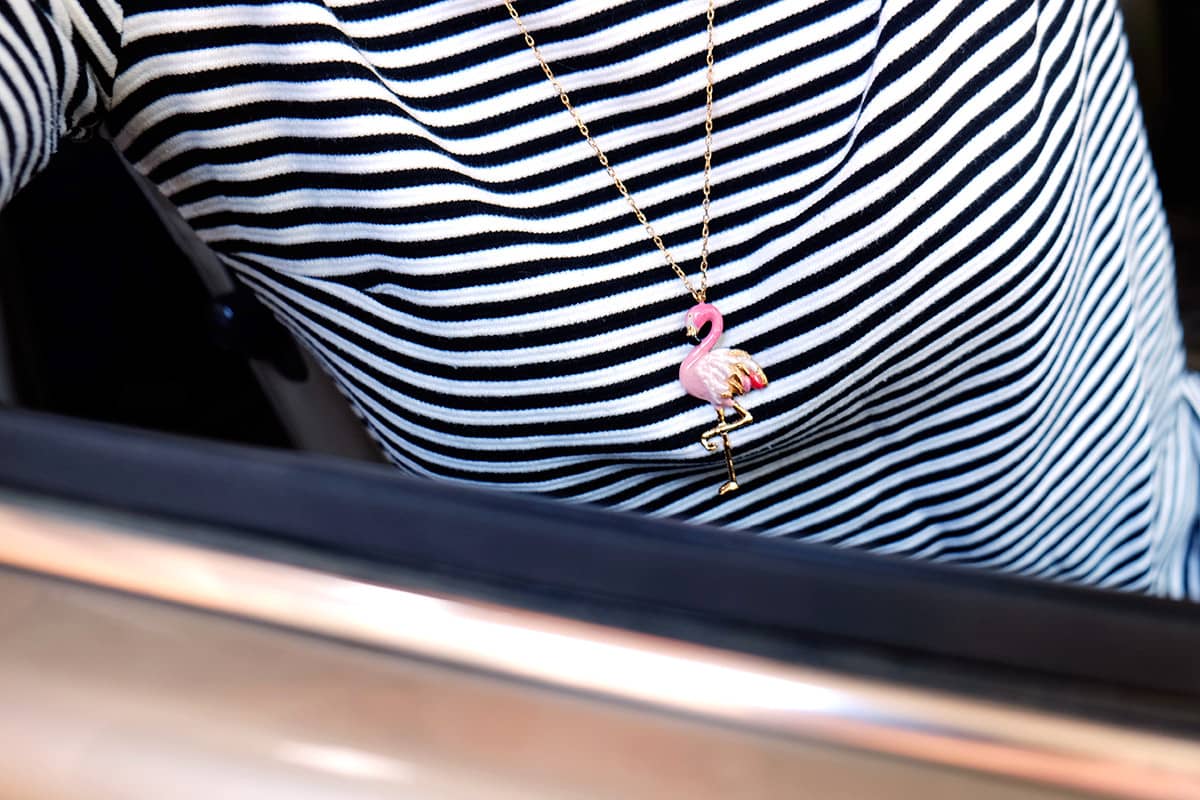 Close-up of a flamingo pendant necklace worn over a striped shirt.