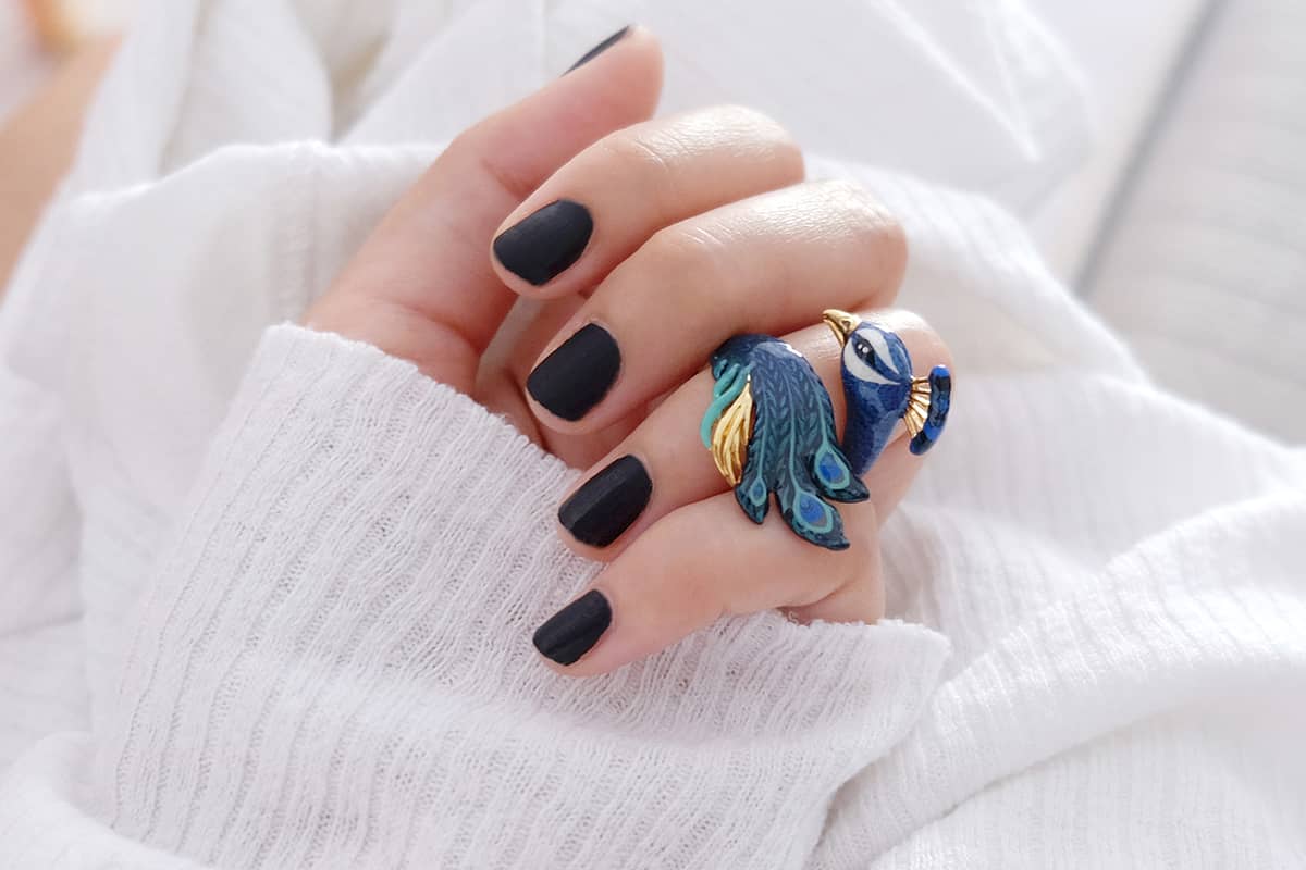 Close up of a hand wearing a stunning peacock ring with intricate details in blue and green.