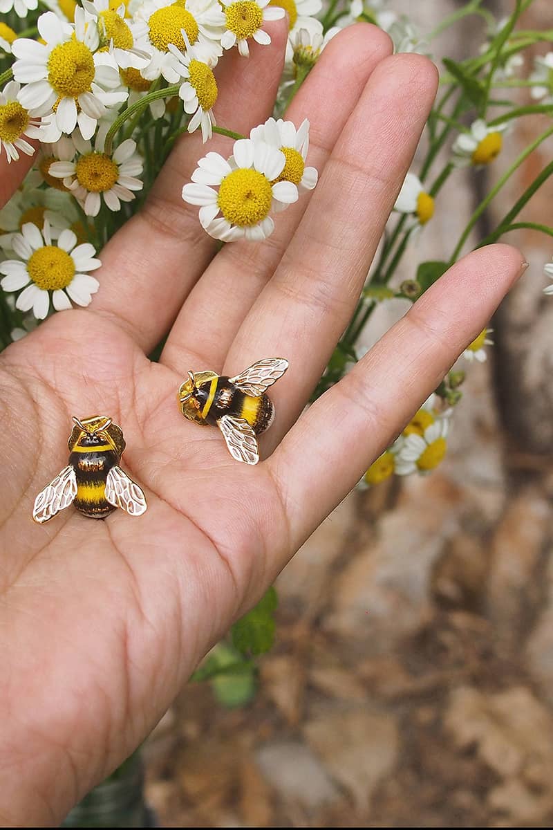 Close-up of bee earrings with daisies in the background