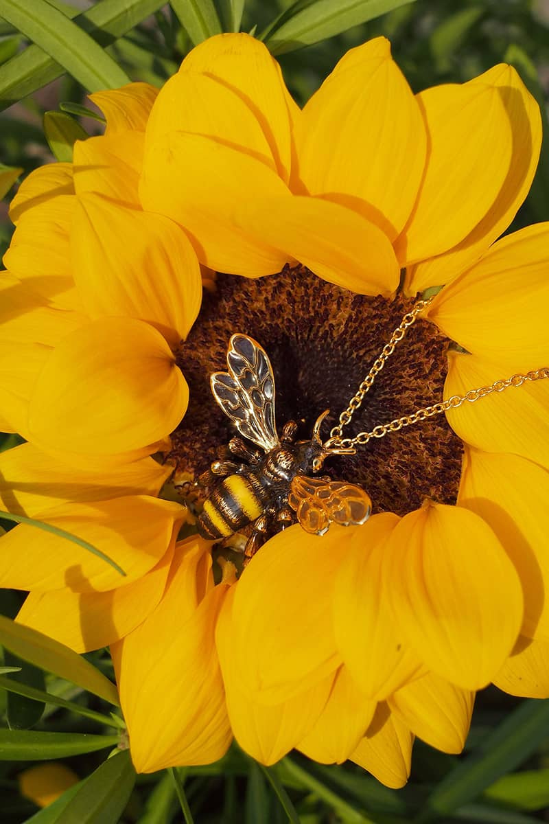 Close-up of a bee necklace resting in the center of a sunflower.