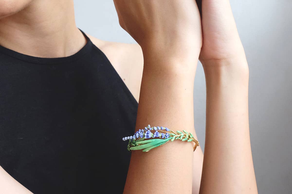 Close up of a model wearing a floral bracelet featuring lavender and green eaves.