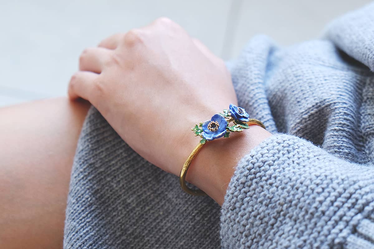 A model wearing a beautiful bangle featuring purple flowers and green leaves details on her wrist.