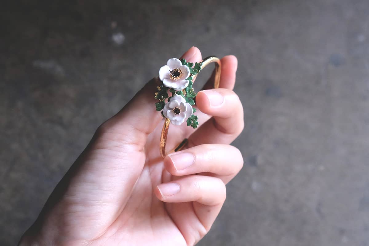 A hand holding a stunning flower bangle with light pink, white flowers and green leaves.