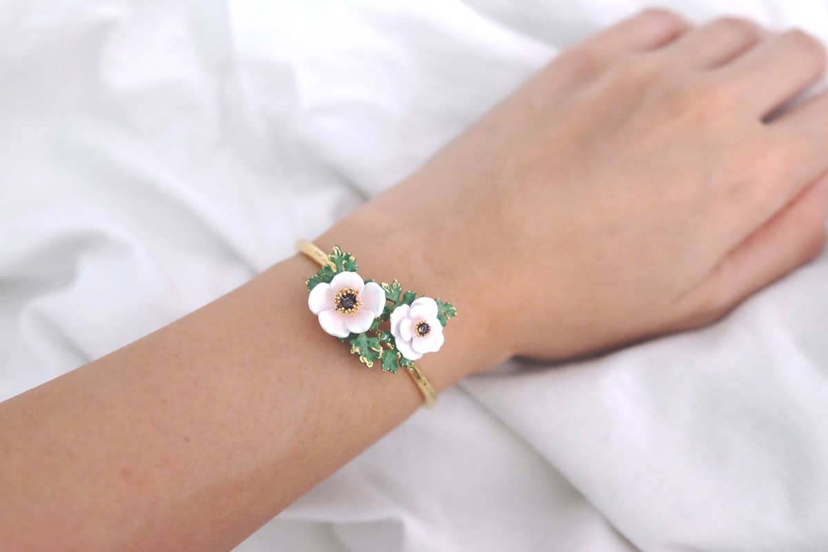 Close-up of a hand wearing a delicate flower bangle featuring light pink, white flowers and green leaves.