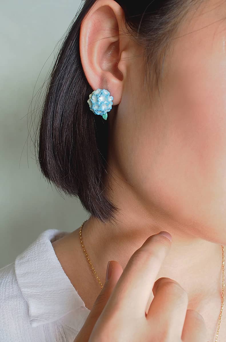 Close-up of blue floral earrings in a woman's ear, highlighting unique jewelry design.