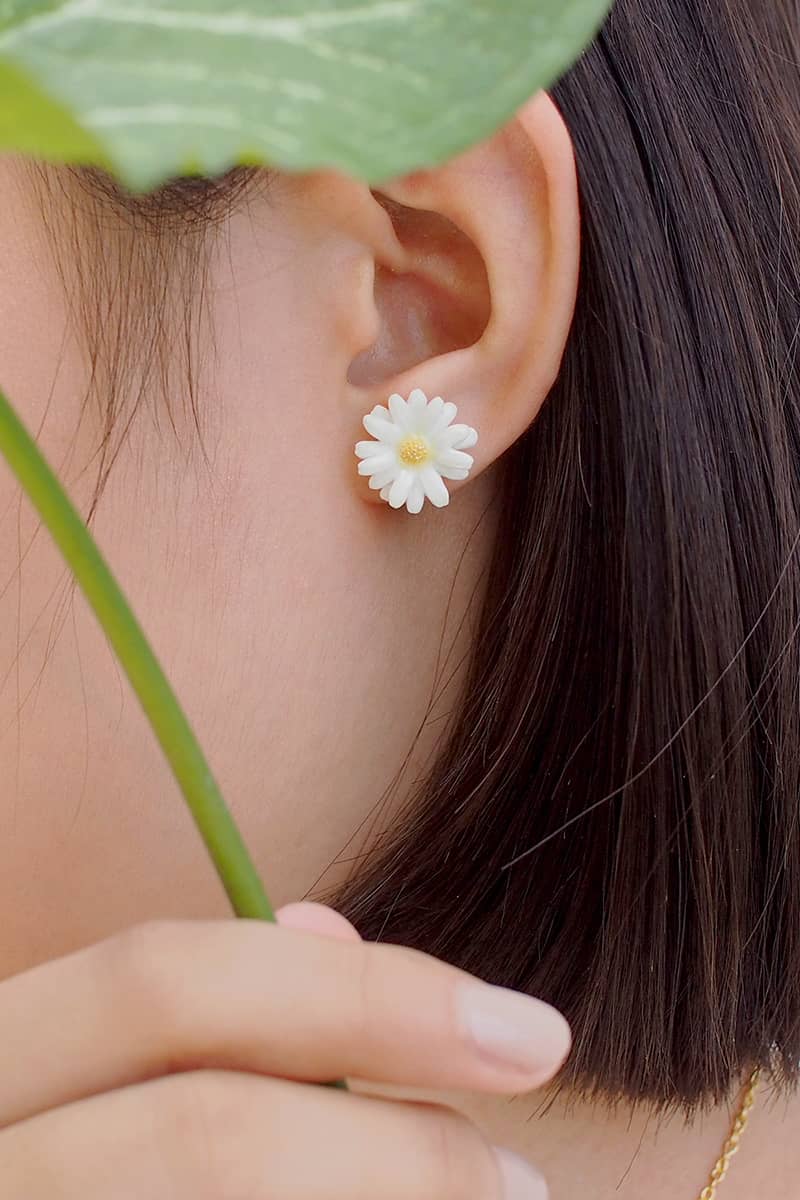 Close-up of a woman's ear adorned with white daisy earrings, perfect for a summer outfit.