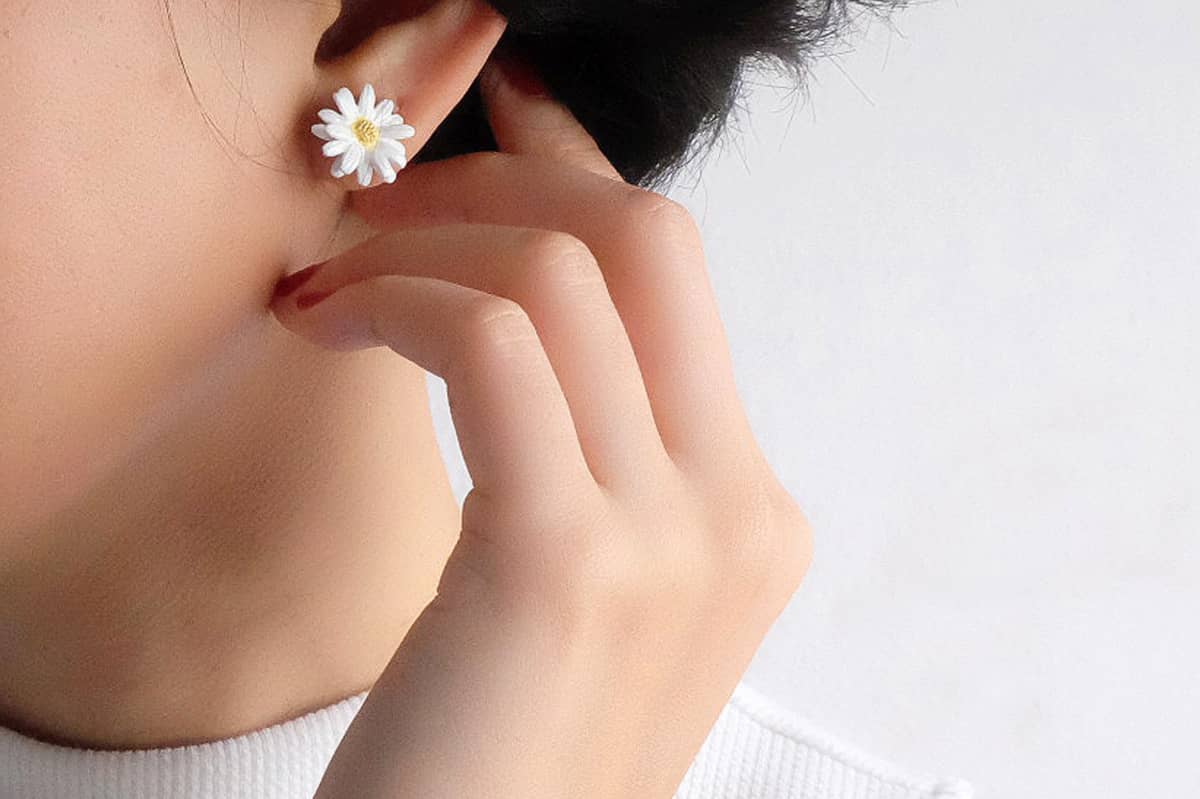 Close-up of a woman's ear adorned with white daisy earrings, perfect for a summer outfit.