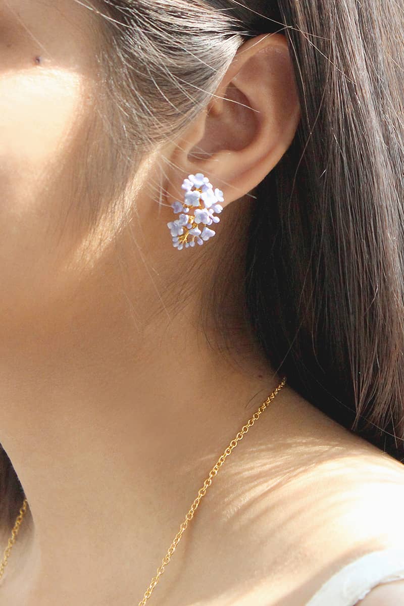 A close-up of a woman's ear adorned with floral earrings featuring light blue flowers and gold accents.