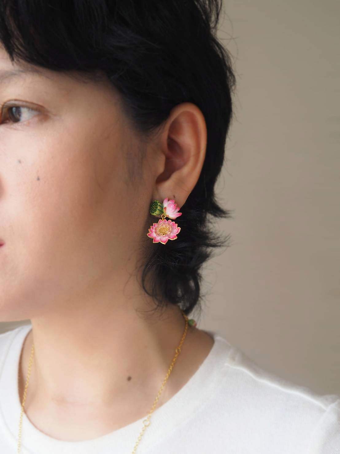 A person wearing floral earrings featuring pink lotus, set against a neutral background.