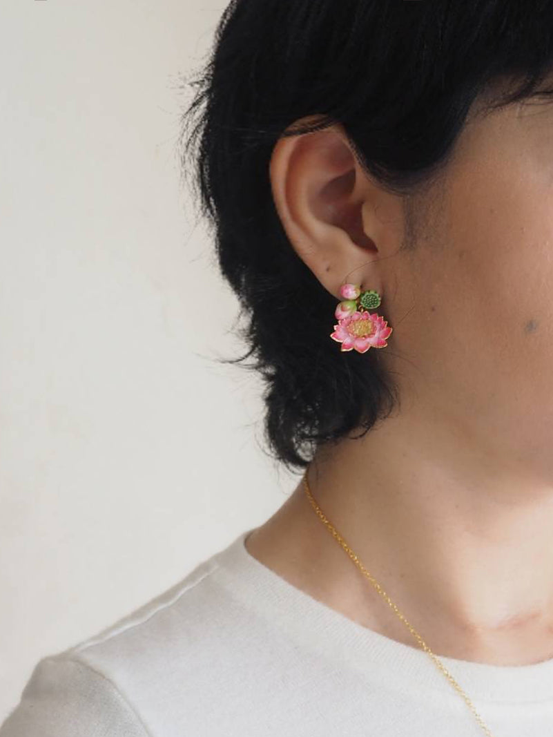 A person wearing floral earrings featuring pink lotus, set against a neutral background.