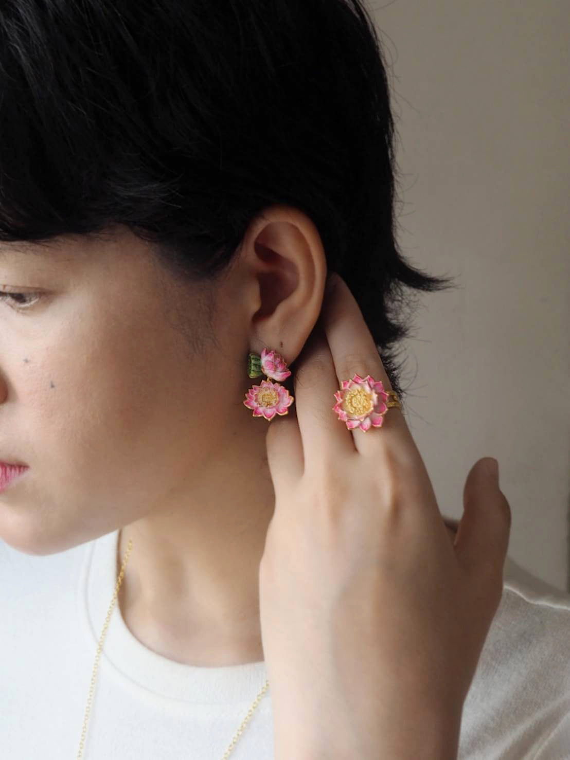 A woman showcases colorful flower earrings and a matching ring while touching her ear.