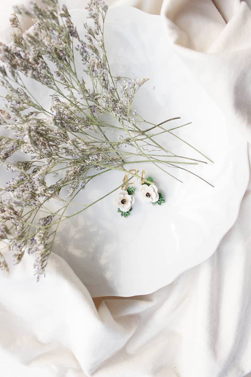 Elegant flower earrings displayed on a white plate with dried flowers.