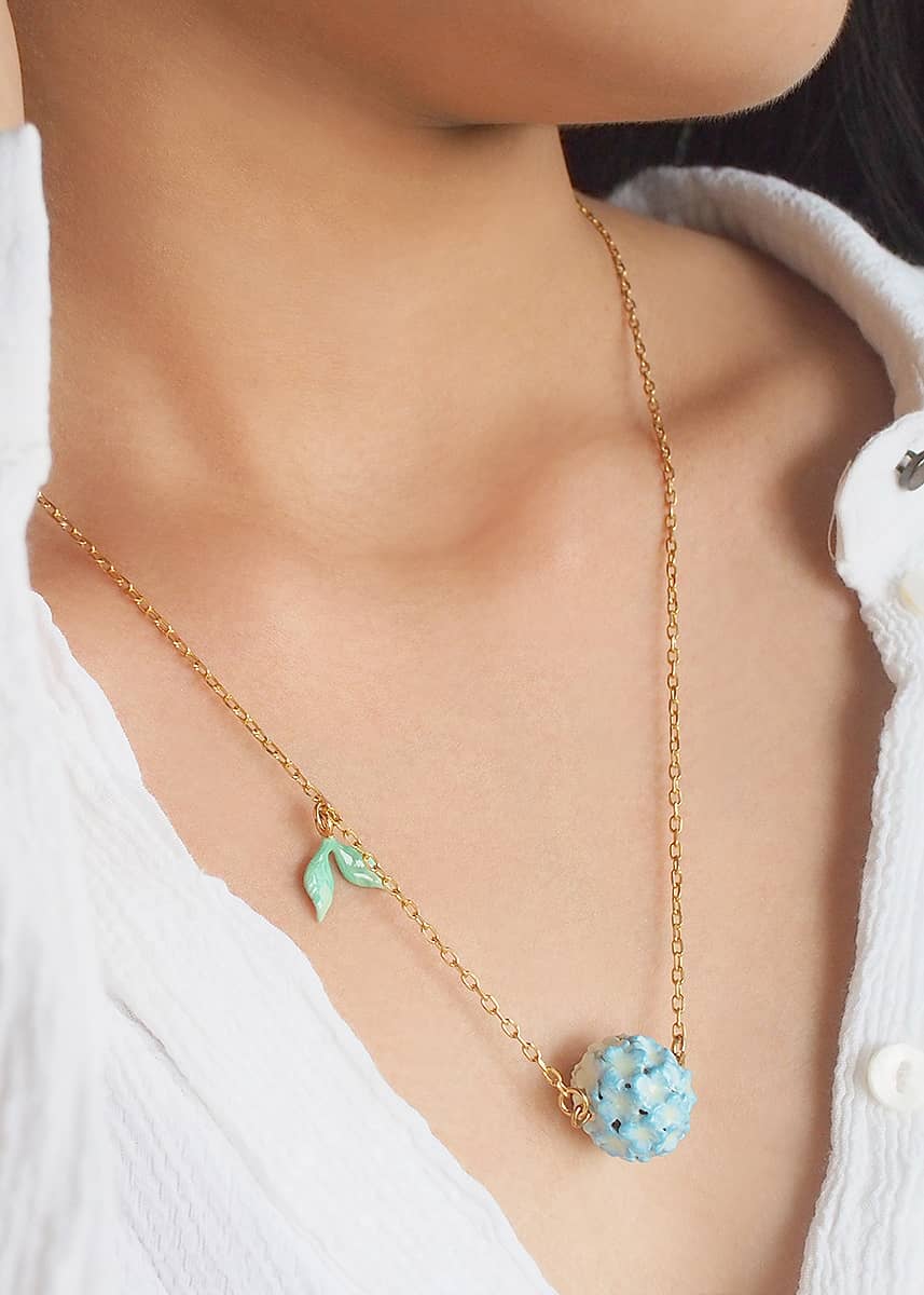 Floral necklace with a gold chain and blue flower pendant with leaf detail worn on a model.