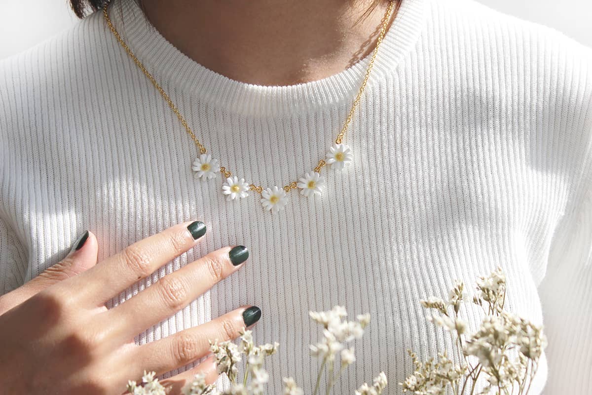 A beautiful daisy necklace with a gold chain worn on a white sweater.