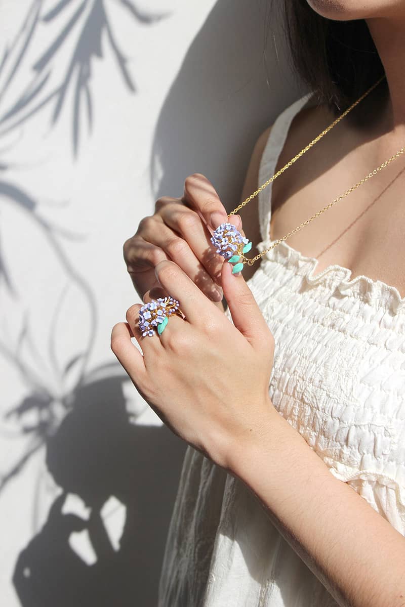 A person holds a floral necklace and shows off floral ring against a softly lit background with shadows.