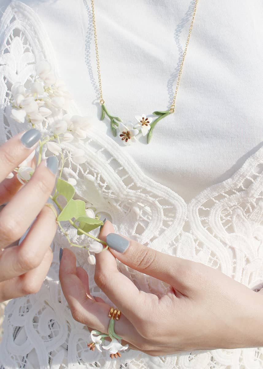 A close-up of hands holding white flowers, adorned with a delicate floral necklace and a lace top.