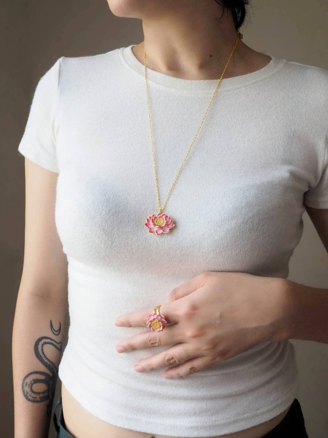 A person wearing a floral necklace, featuring a pink lotus pendant, and a matching ring.