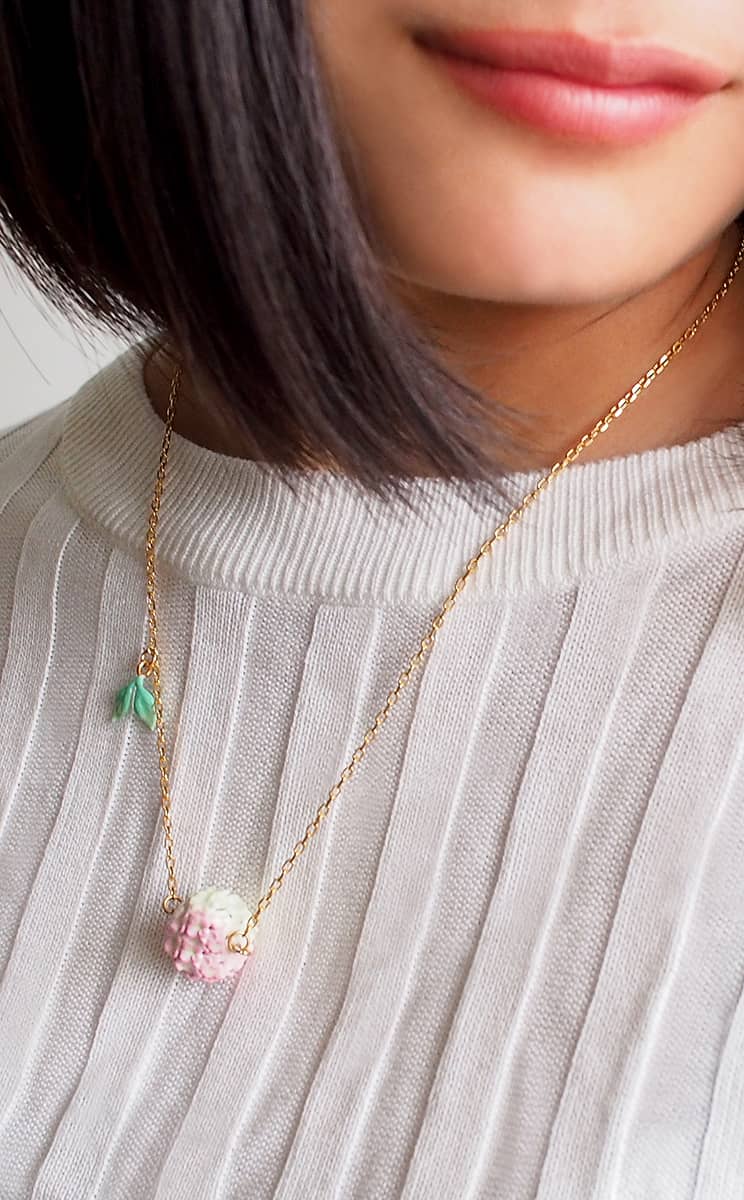 Floral necklace with a gold chain and soft pink flower pendant with leaf detail worn on a woman.