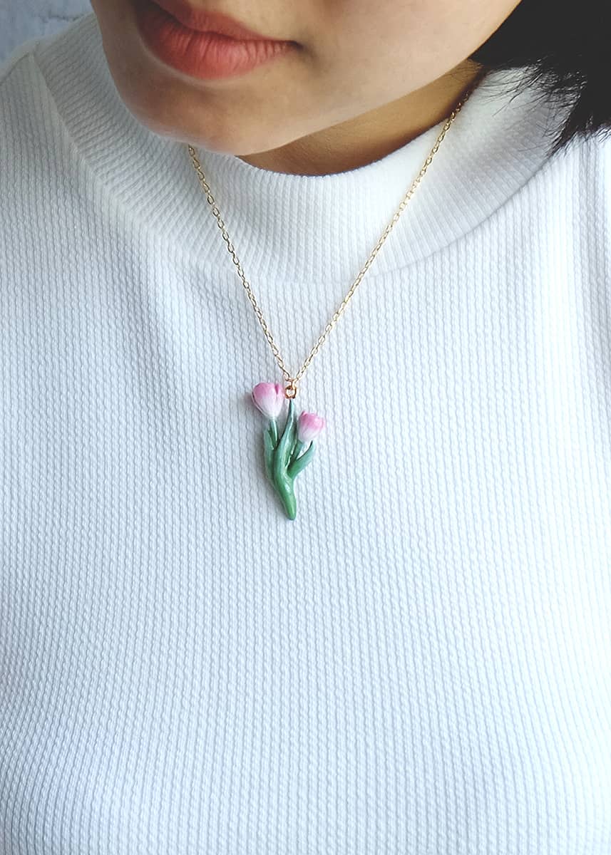 Close-up of a person wearing a cute tulip necklace white a white top.