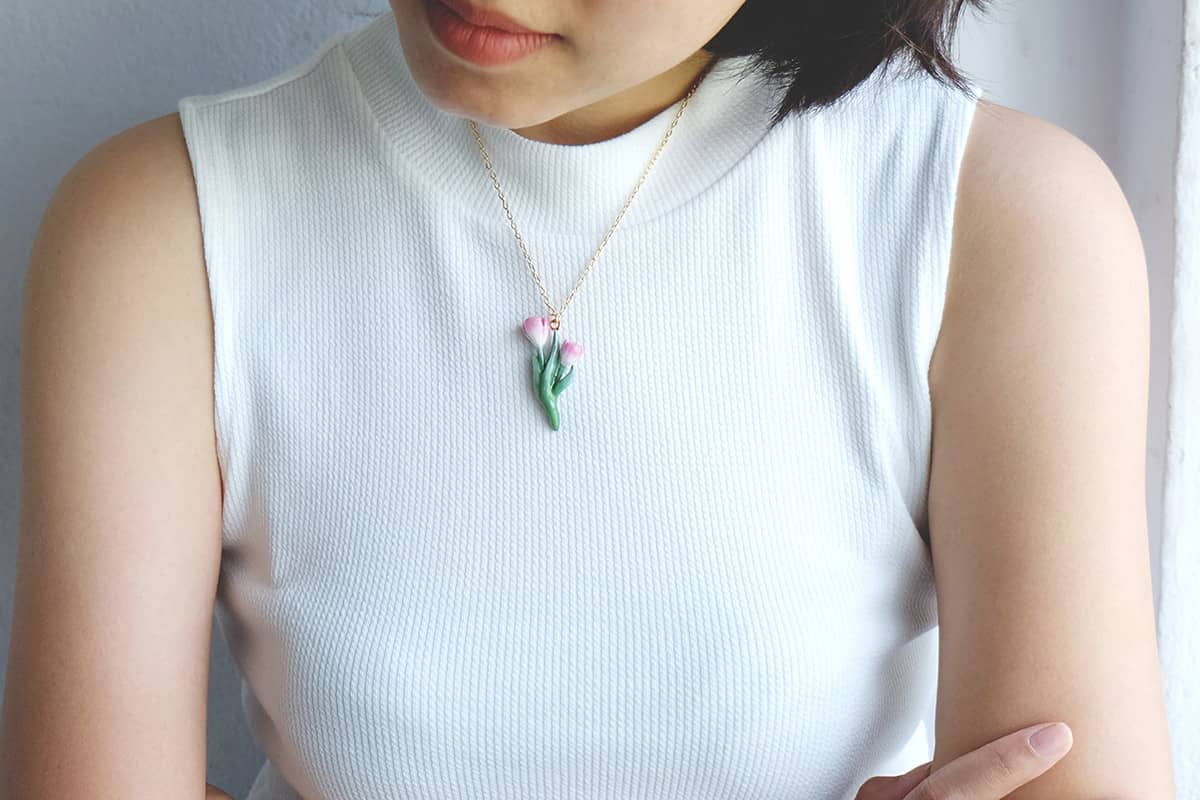 Close-up of a person wearing a cute tulip necklace white a summer outfit.