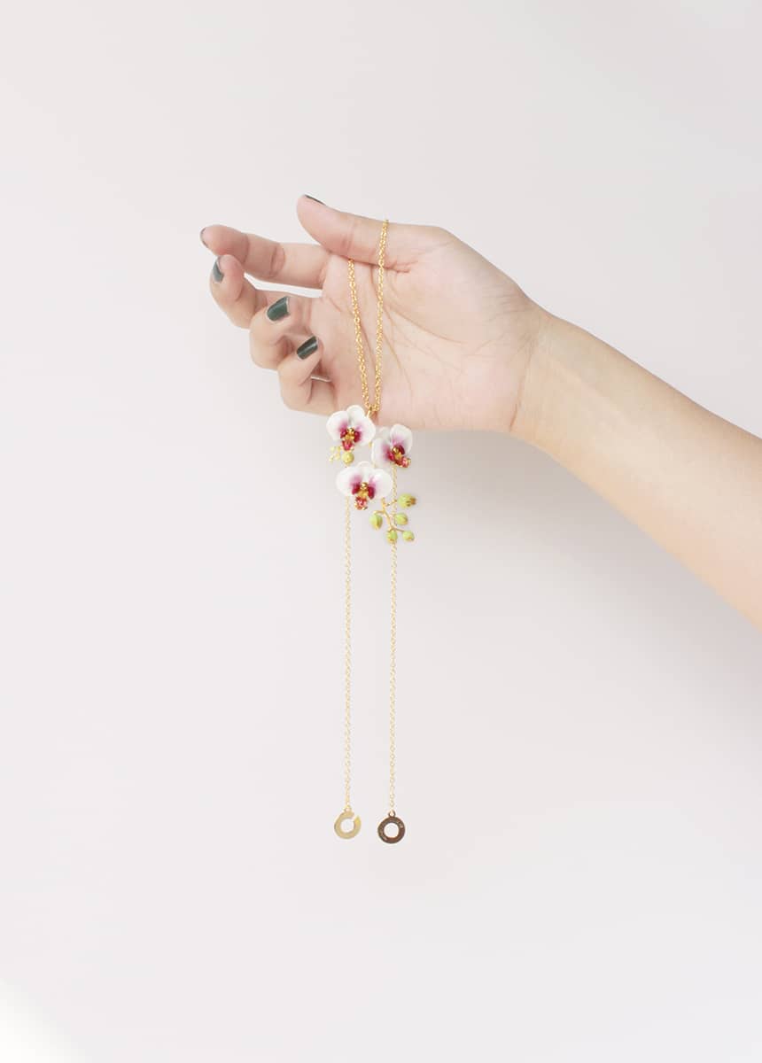 Close up of a hand holding a gold necklace with three white flowers and golden accents pendant.