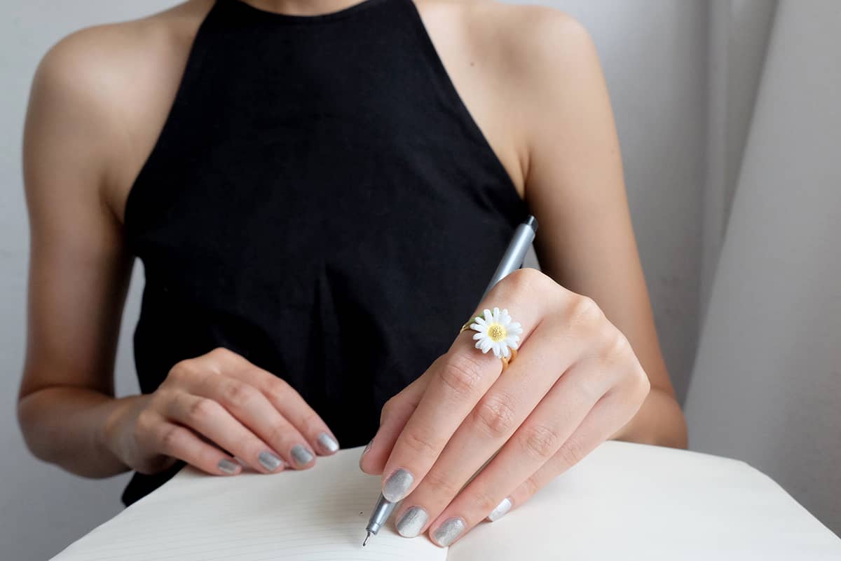 Close-up of a hand with a daisy ring while writing on a notebook.