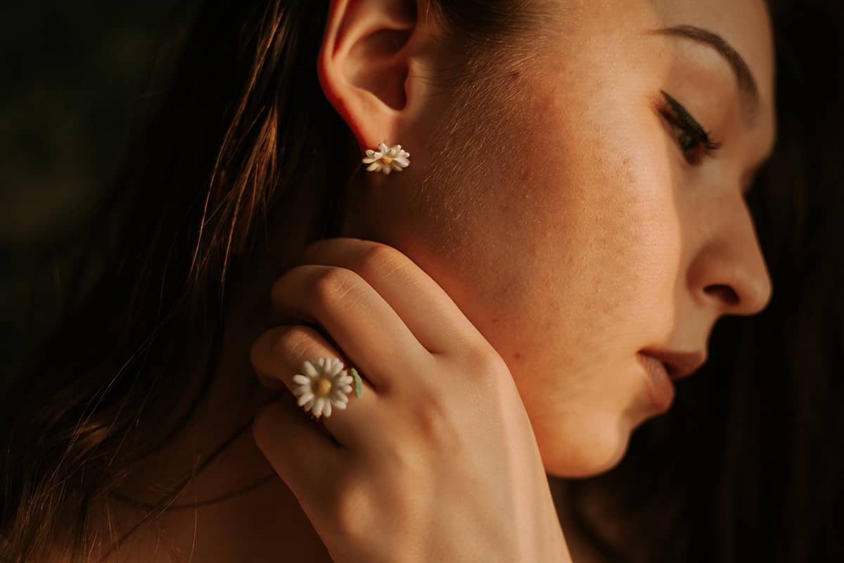 Close-up of a woman wearing flower earrings and a matching ring, showcasing delicate jewelry.