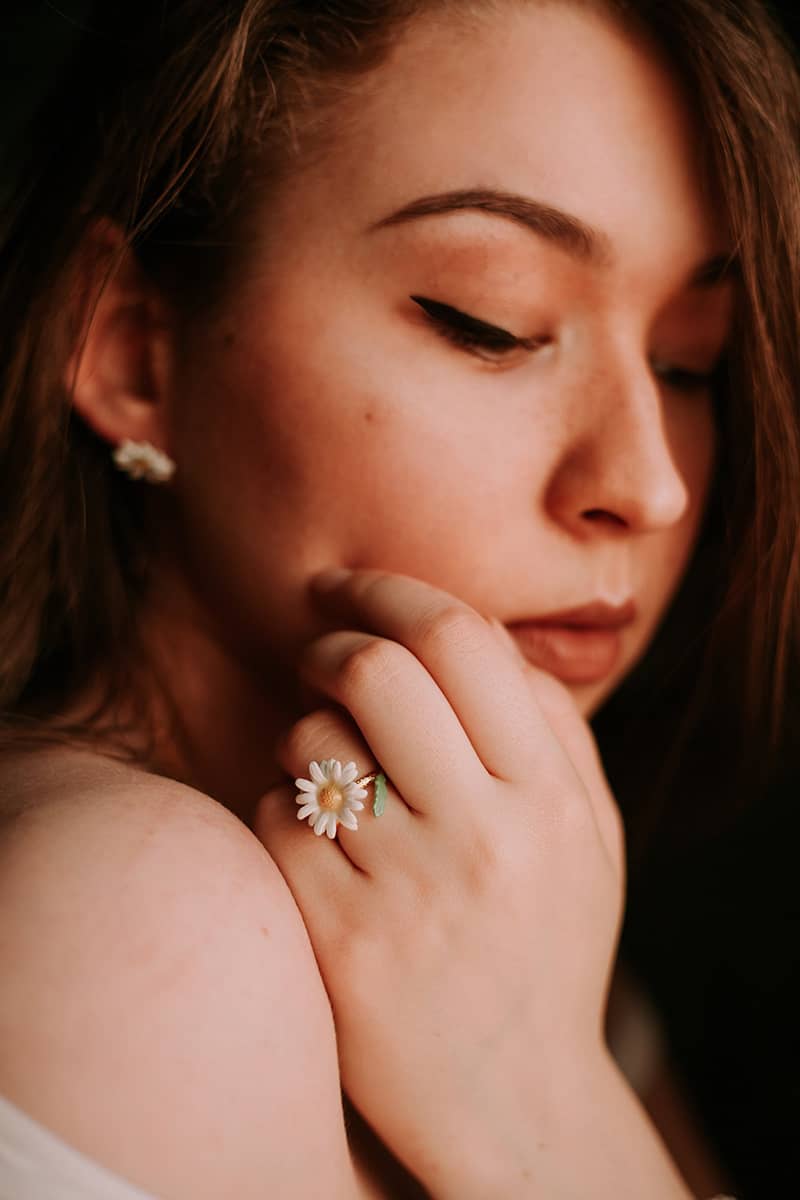 Close-up of a woman wearing flower earrings and a matching ring, showcasing delicate jewelry.