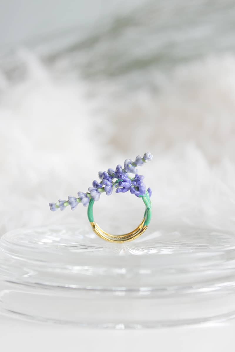 A beautiful gold ring featuring delicate lavender flowers and green leaves place on a light background.