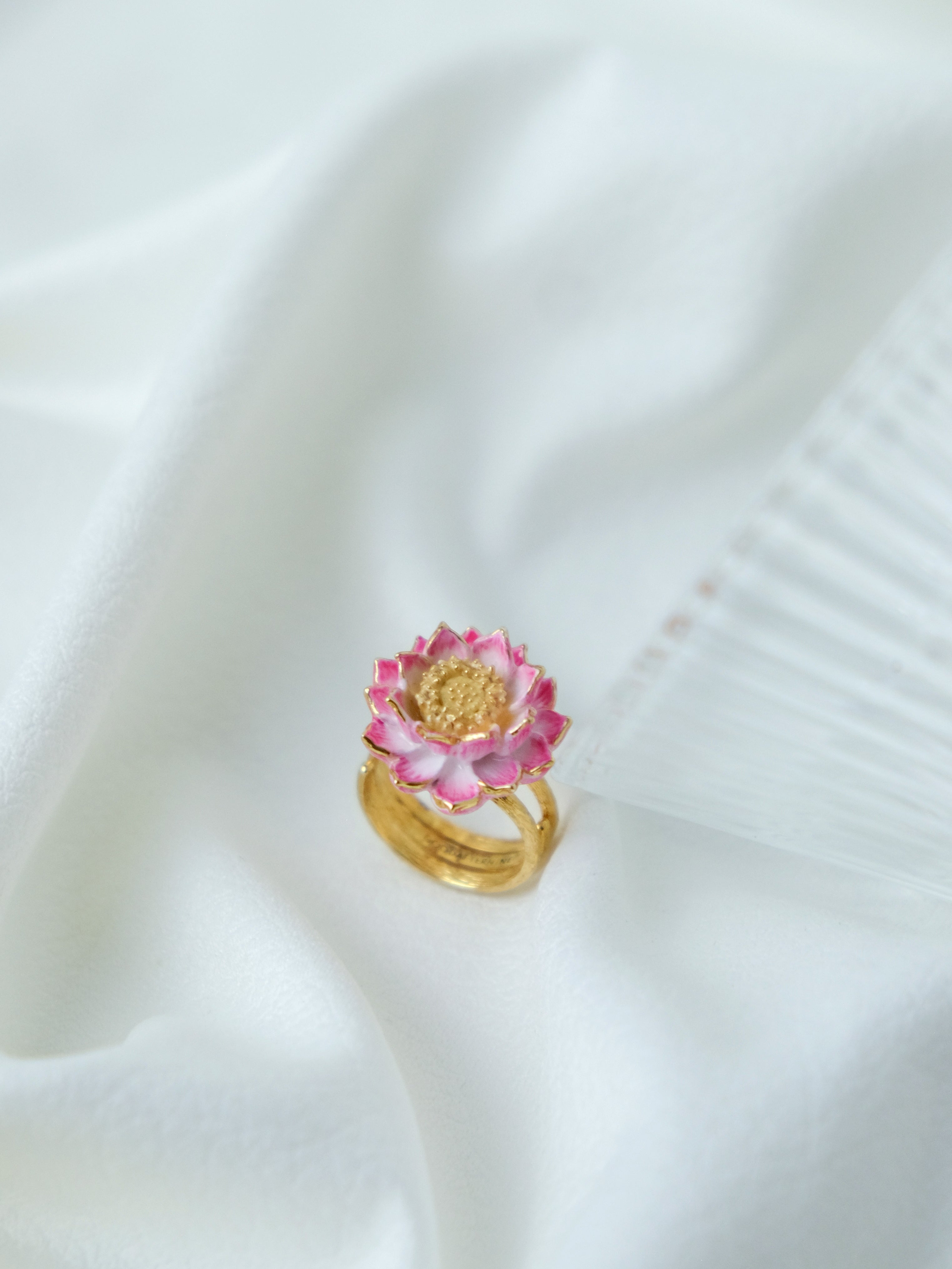 A charming floral ring showcasing a pink lotus flower, placed on white fabric.