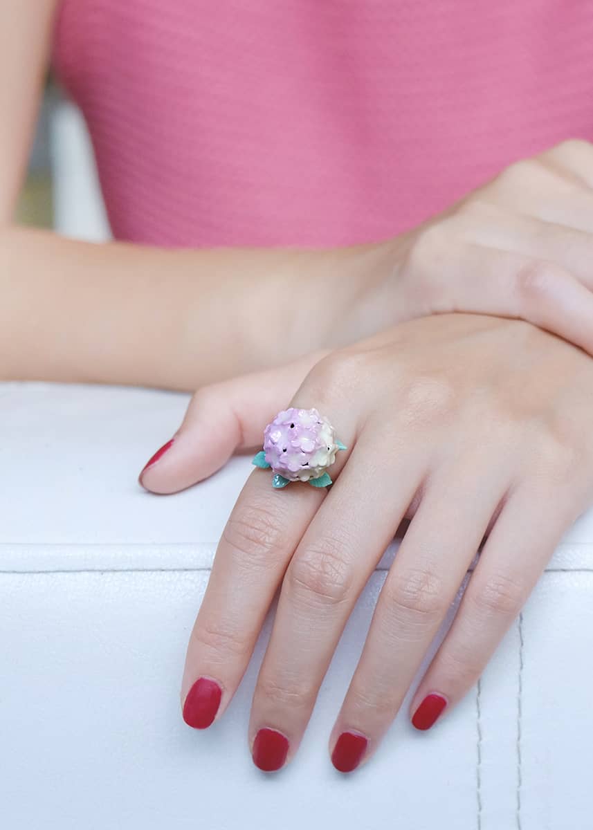 Close-up of a hydrangea flower ring on a hand with red nails.