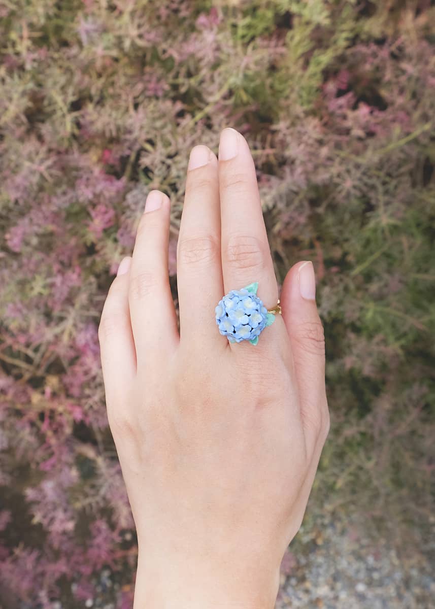 A hydrangea ring displayed on a hand in a natural setting.