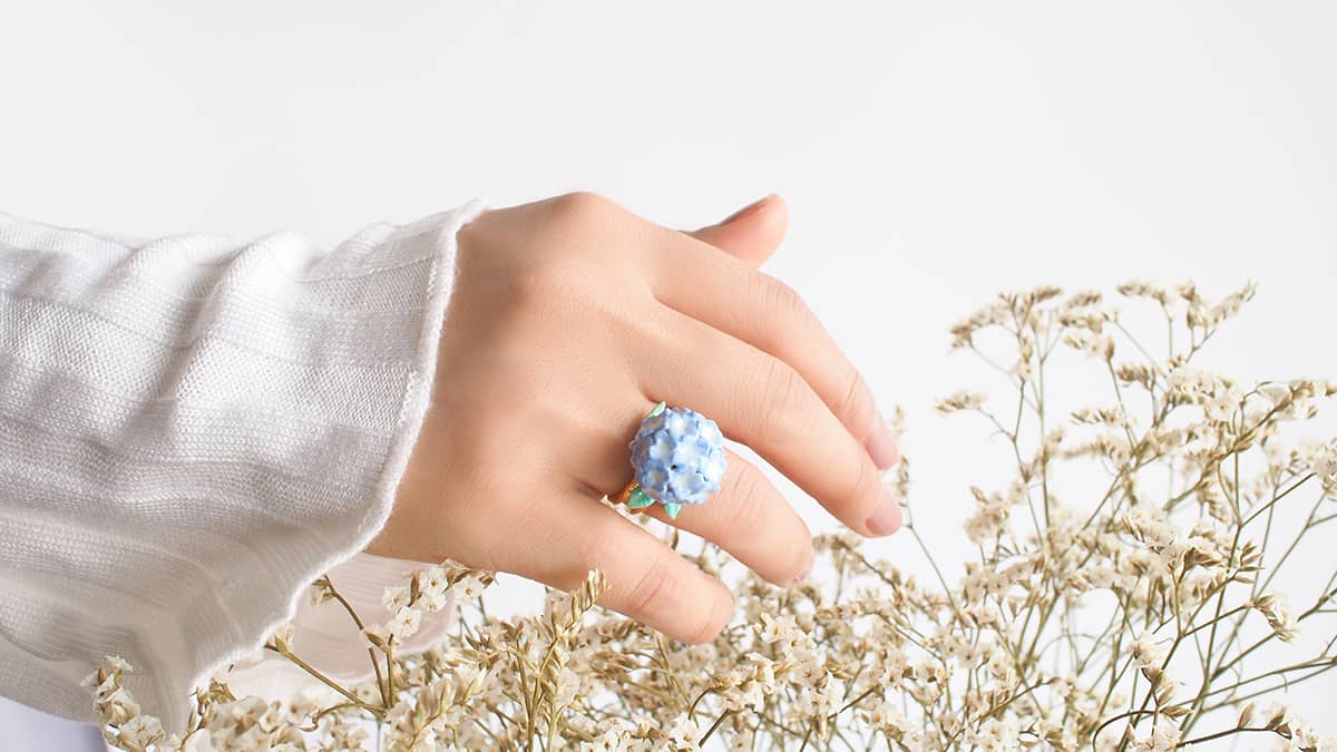 A hand showcasing a beautiful hydrangea ring amidst dried flowers.