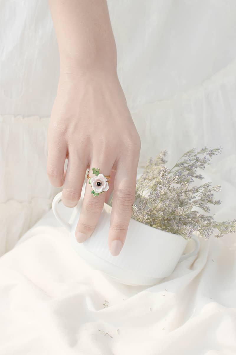 Close-up of a hand wearing a delicate light pink flower ring holding a white cup with flowers.