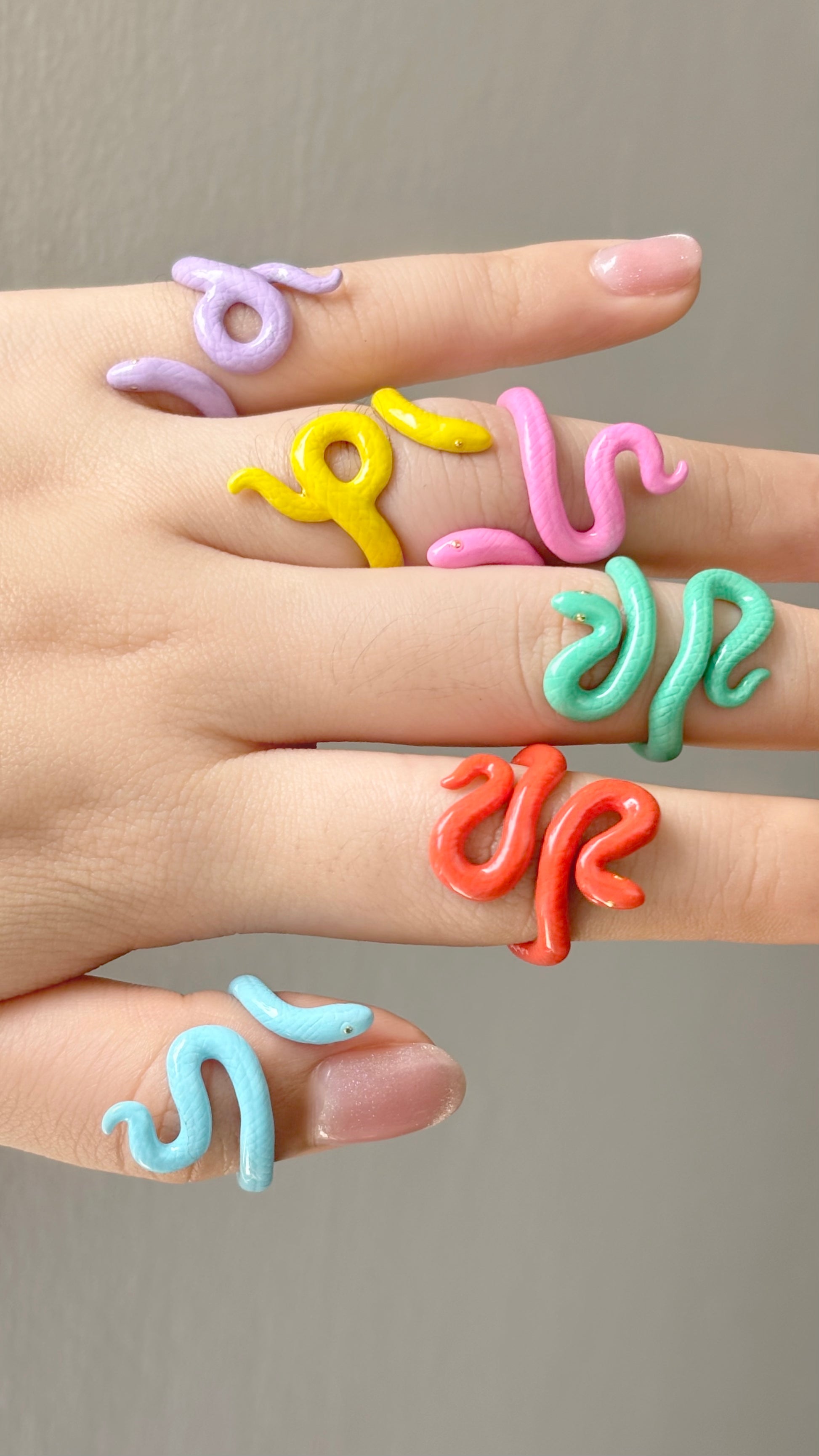 A variety of colorful snake-shaped rings worn on fingers.