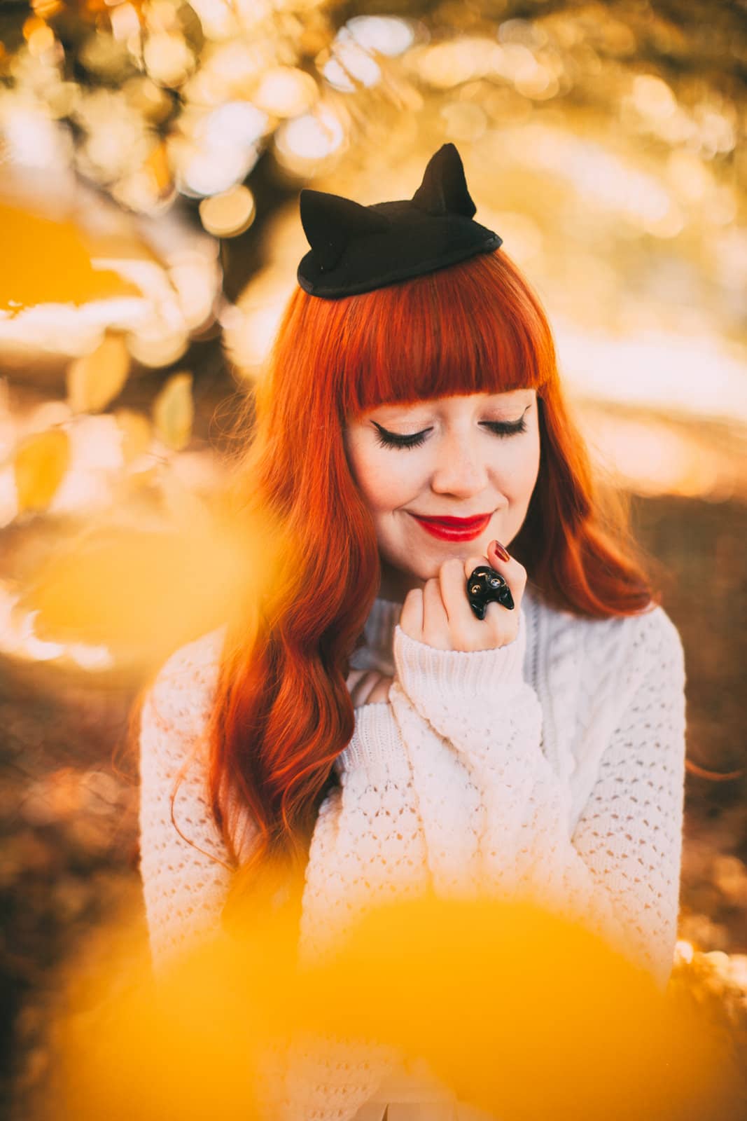 Black cat ring worn by a person in a sweater in field of autumn.