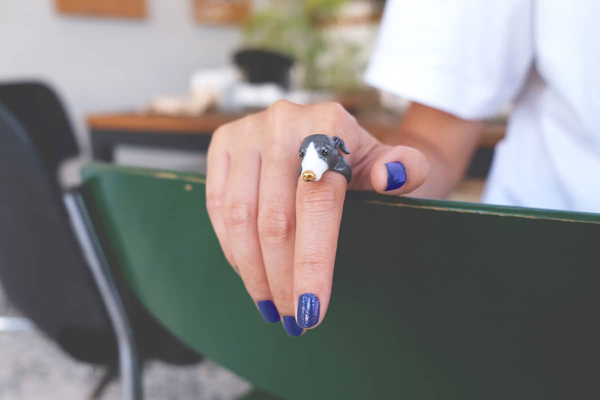 A close-up of a hand with an adorable dog ring places on a back of a chair.