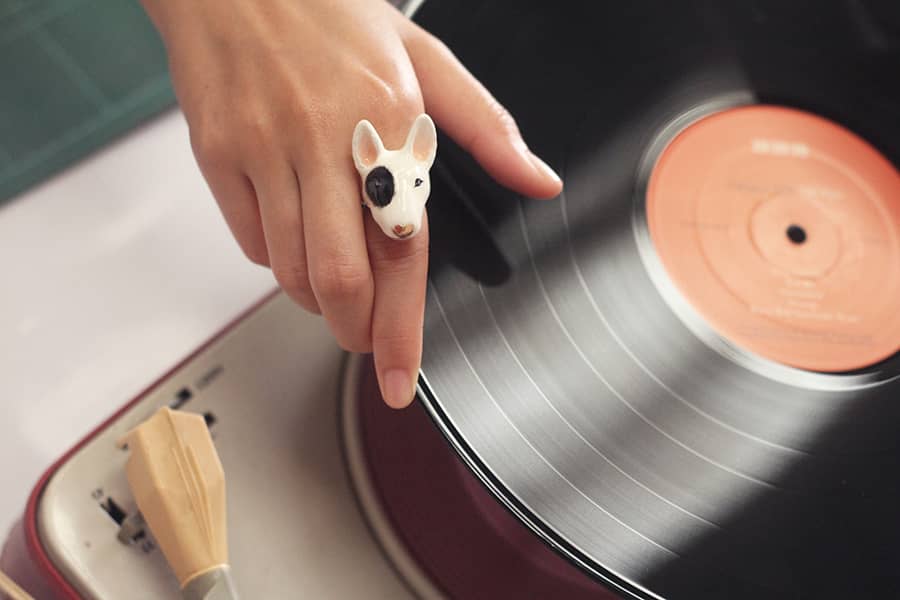 A hand wearing a cute Bull Terrier dog ring while next to a spinning vinyl.