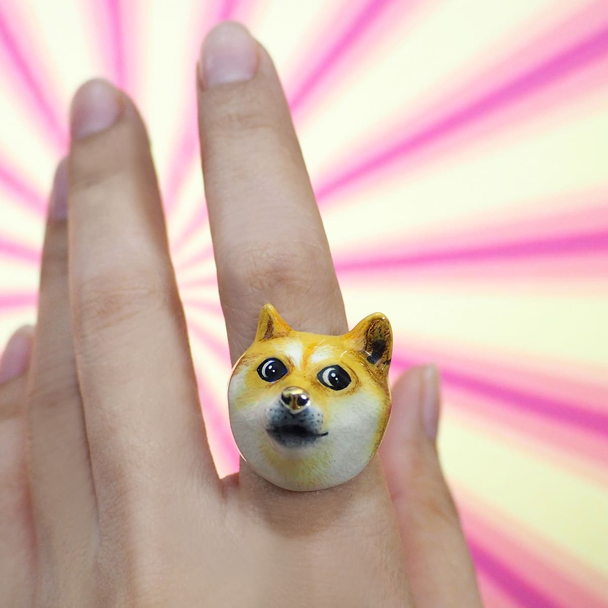 Hand wearing a doge face ring with a colorful background.