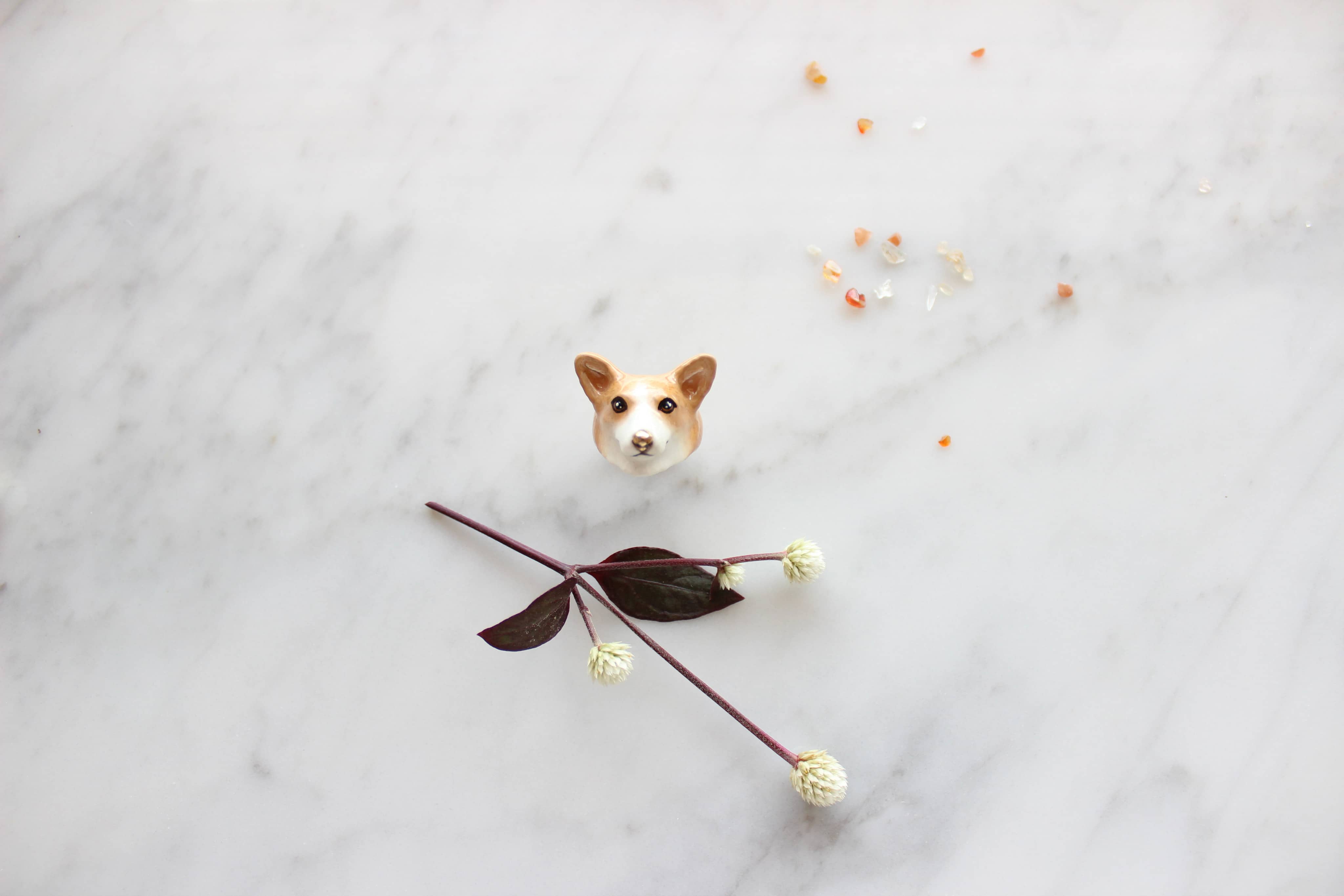 A cute, hand-painted ring featuring corgi head placed on marble background.