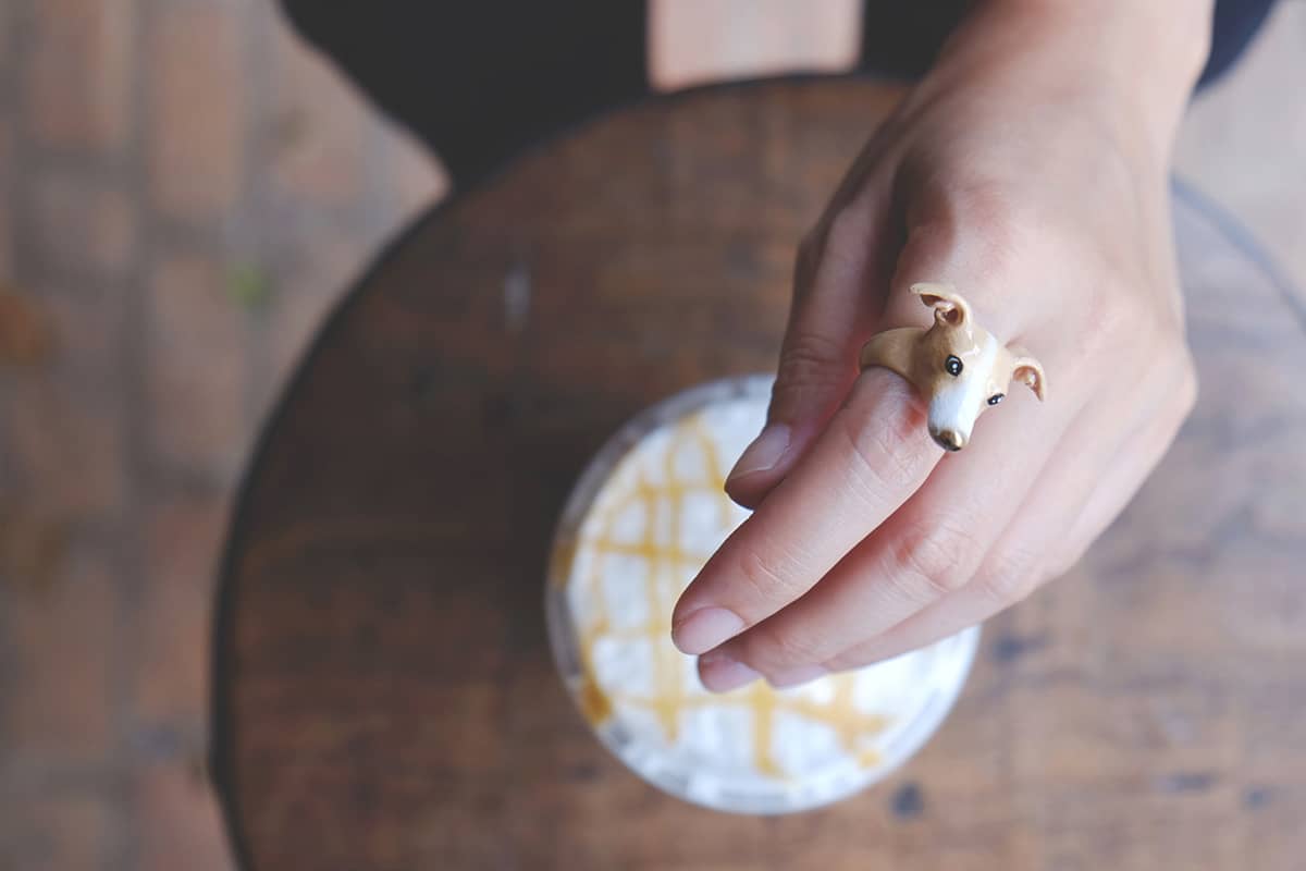 A close-up of a dog ring worn on a hand with a cap of coffee set in the background.