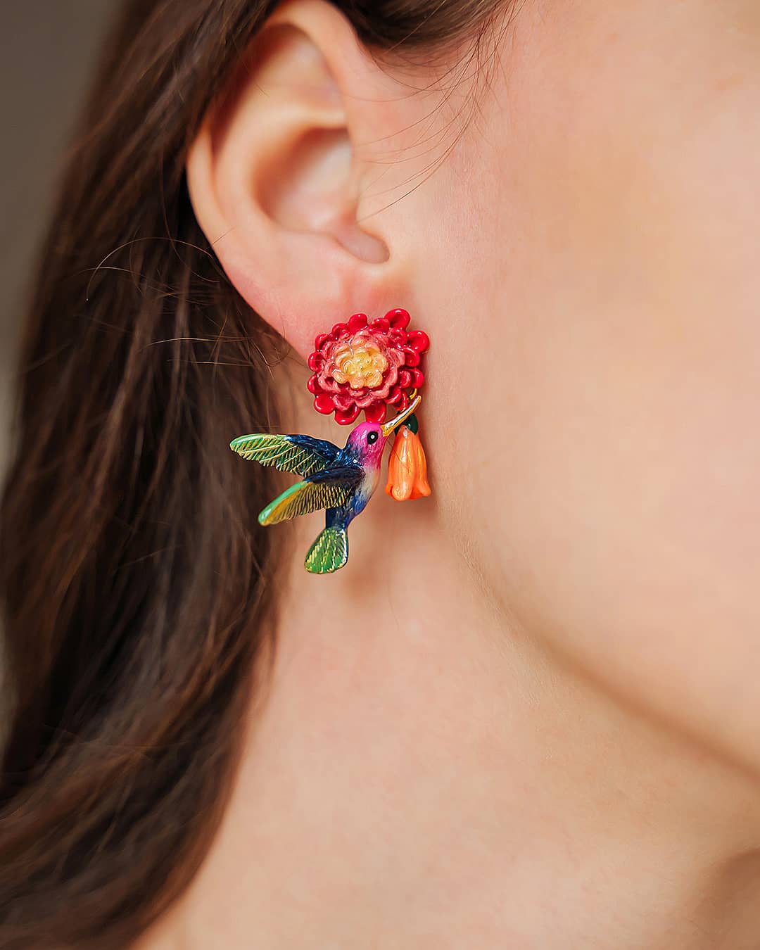 Close-up of stunning hummingbird earrings with floral design worn on the ear