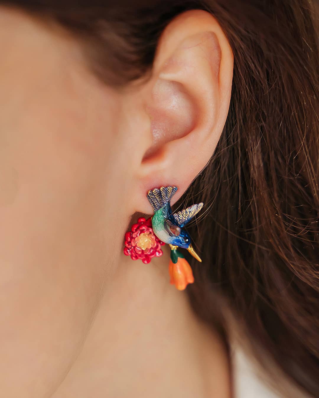 Close-up of vibrant hummingbird earrings with floral design worn on the ear