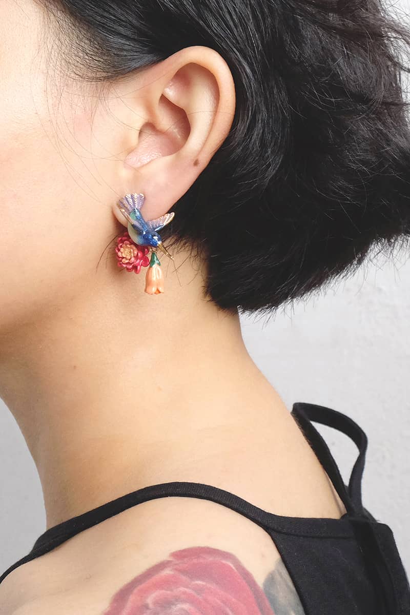 Close-up of vibrant hummingbird earrings with floral design worn a model's ear