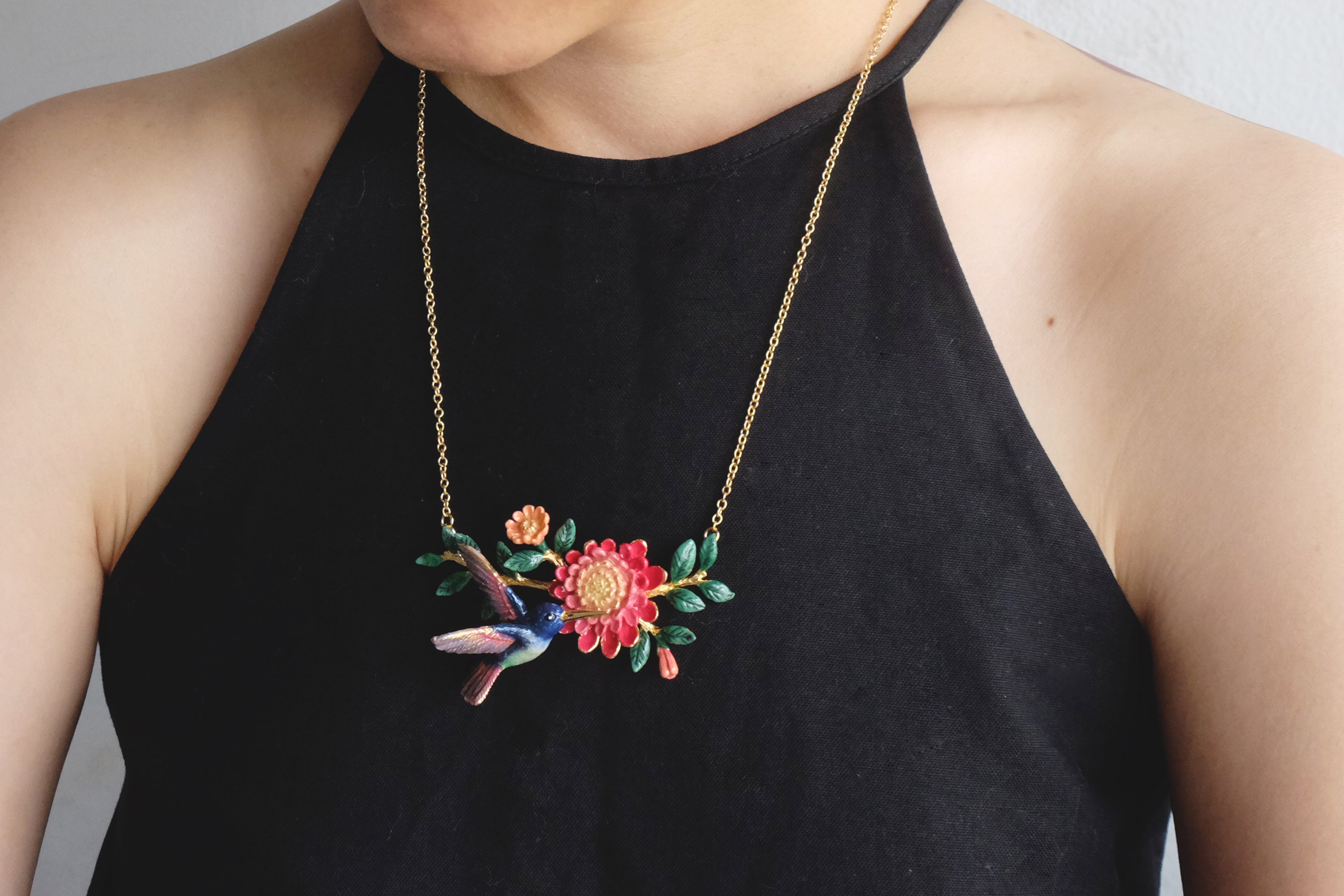 Close-up of a unique necklace featuring a hummingbird and floral design worn on a black top.